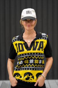 Woman in a black and gold vintage University of Iowa Hawkeyes shirt and matching hat, smiling during a rooftop personal branding photoshoot in Iowa City.